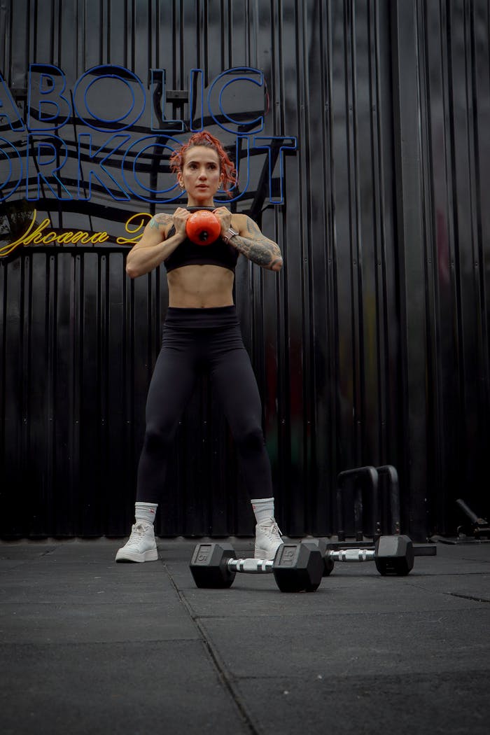 Tattooed woman exercises with kettlebell at a gym in Ciudad de México, achieving fitness goals.